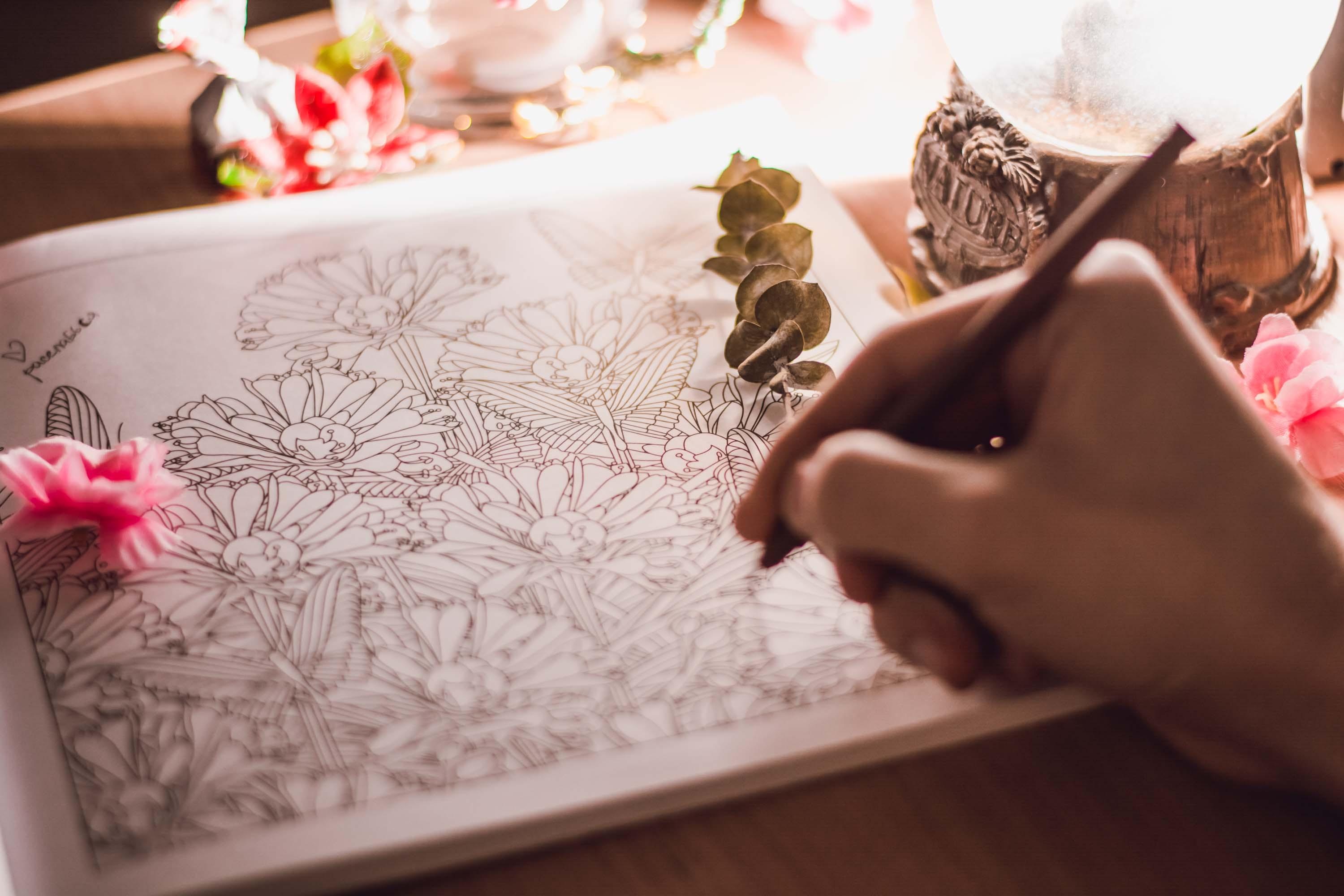 hand holding colored pencil draws on coloring page in coloring book