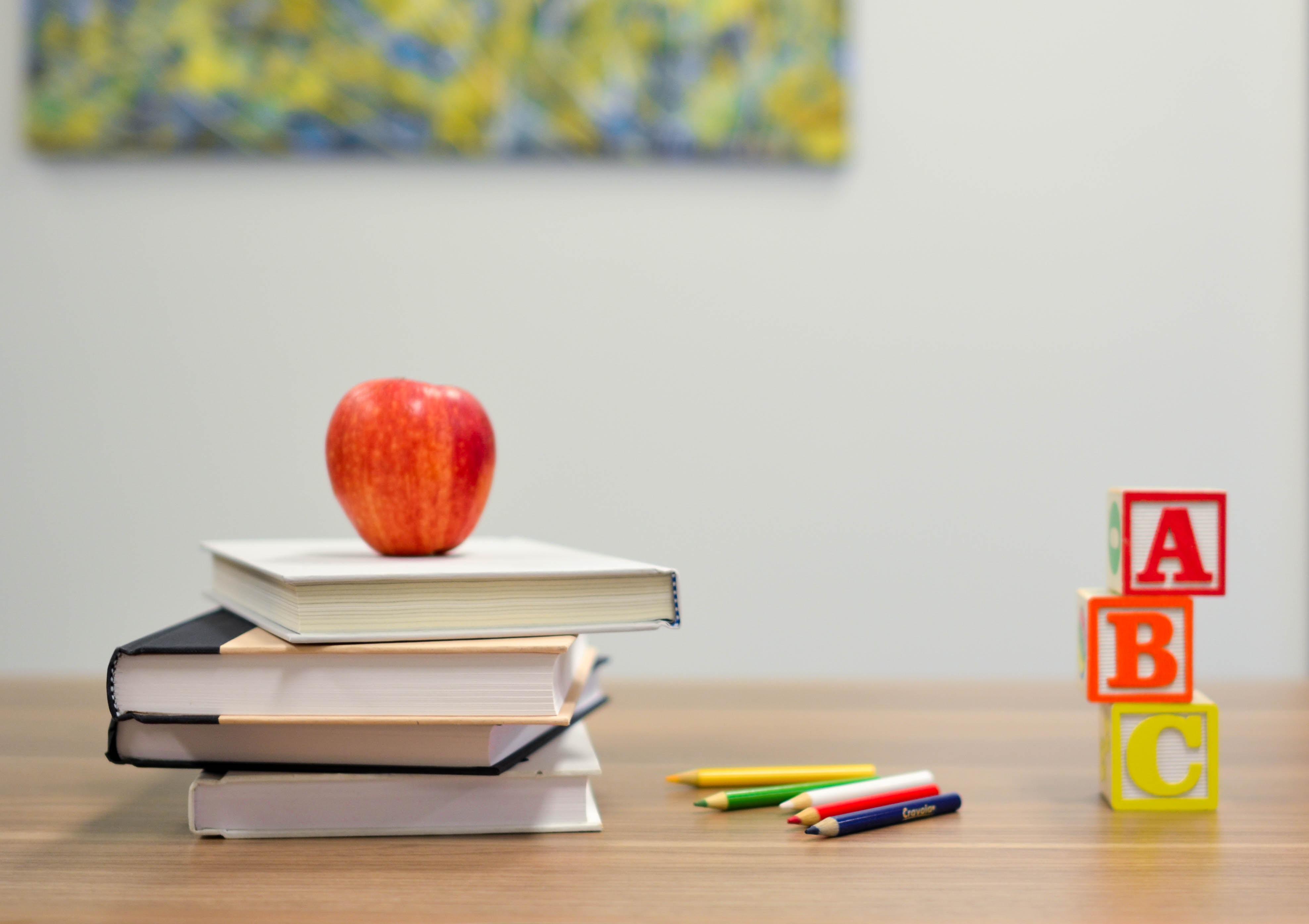 an apple sits on top of a stack of books next to a pile of colored pencils and ABC blocks