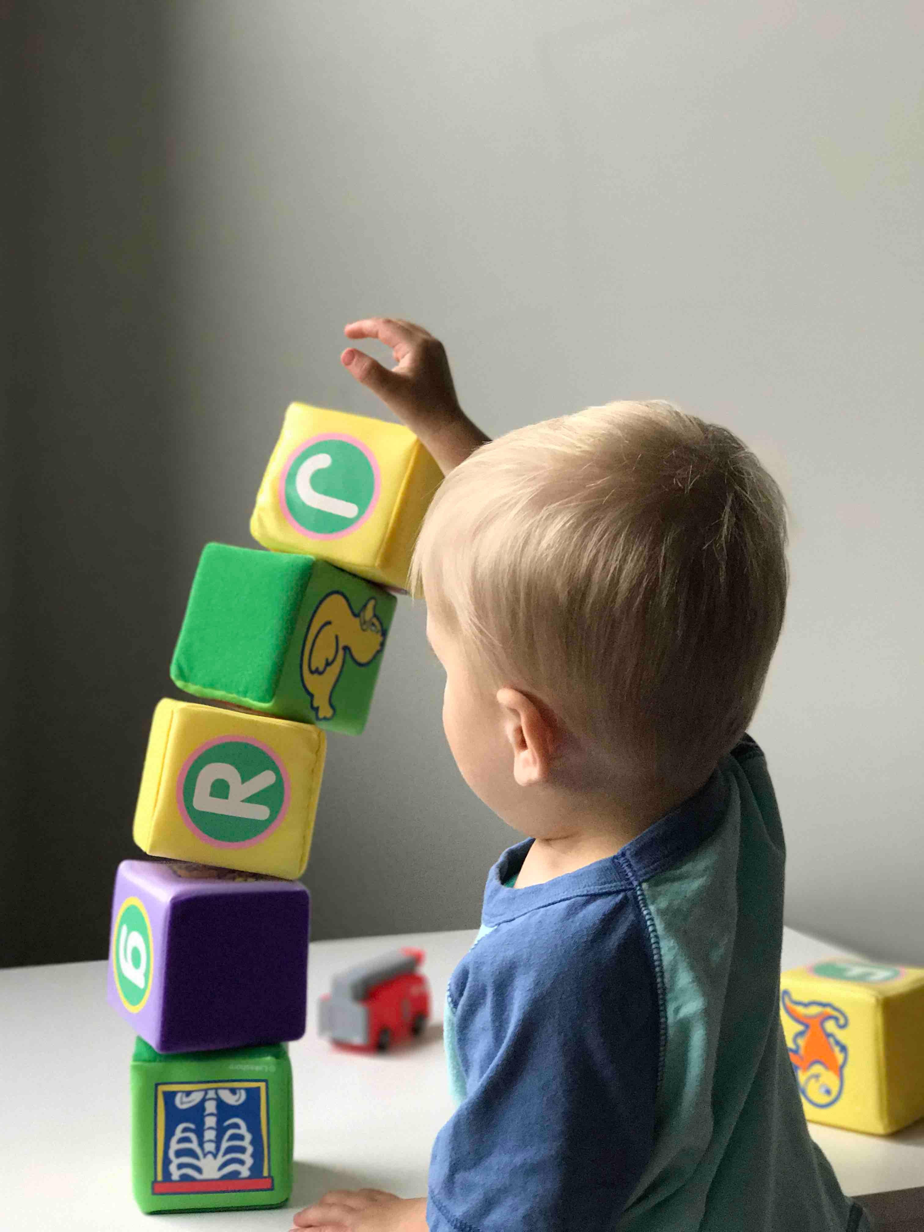 a child with blond hair stacks colorful blocks