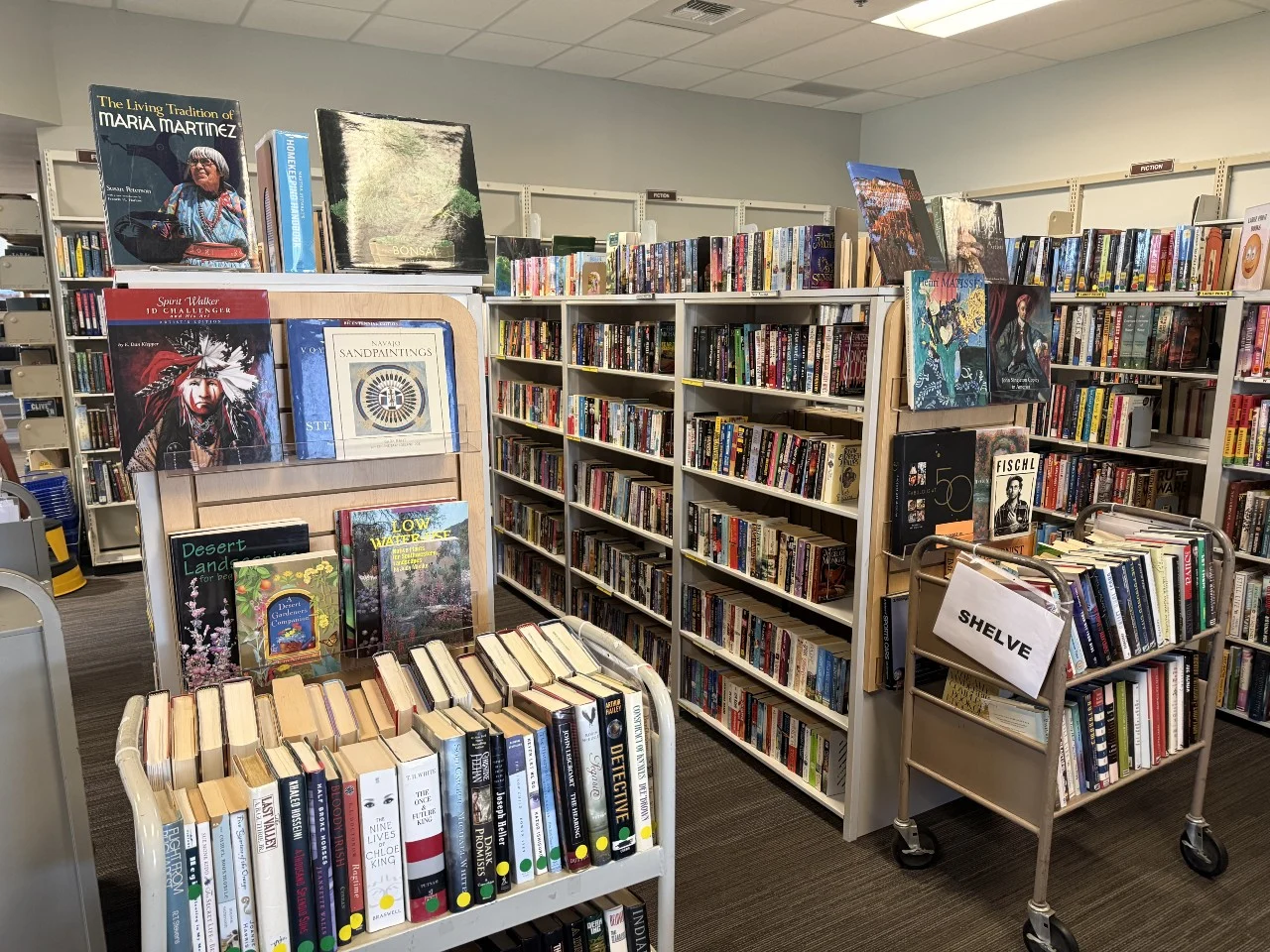 Library interior with bookshelves filled with various books and a cart labeled Shelve.